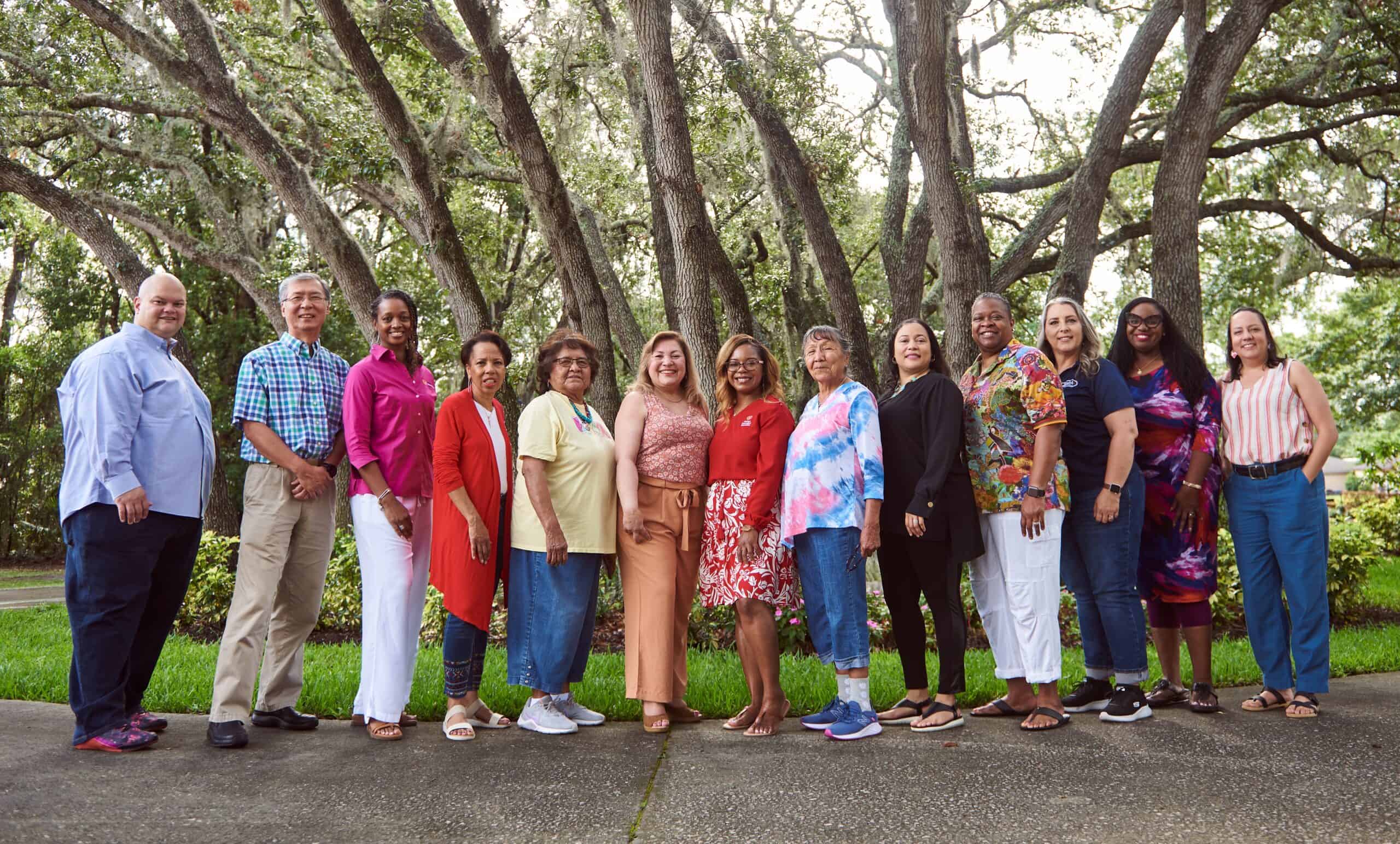 Group of people standing together in front of a tree looking towards the camera. 